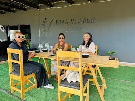 Guests seated at a wooden table on the Eraa Village garden patio, with the Eraa Village sign in the background